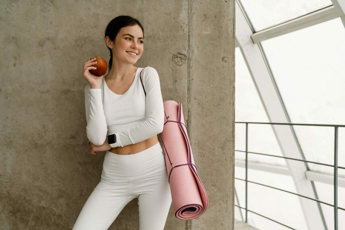 Young smiling woman holding yoga mat while standing with yoga mat